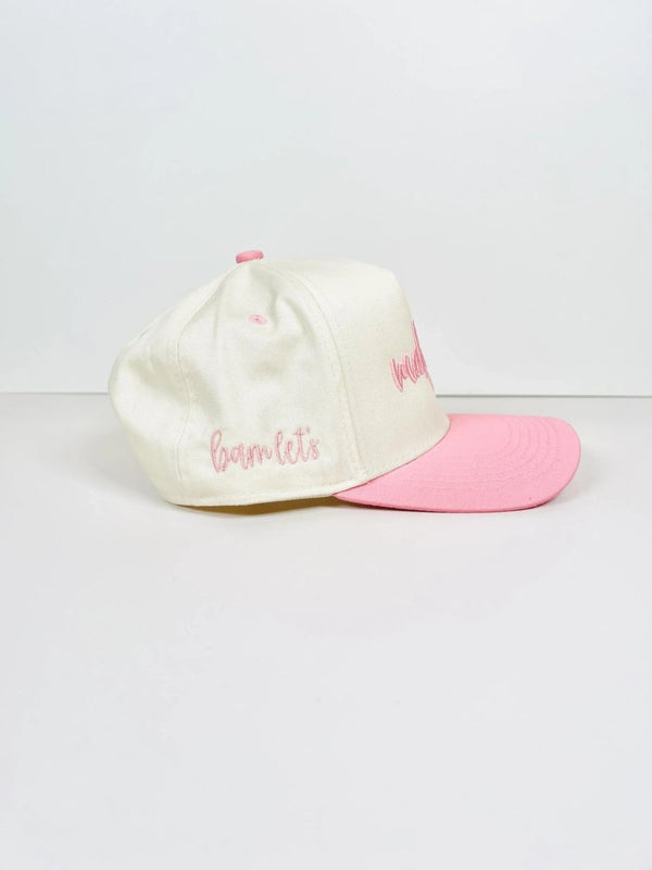Side view of a cream and pink Mahjong trucker hat with 'bam let's' embroidered in pink cursive on the side. The cap features a structured front panel and a pink brim.